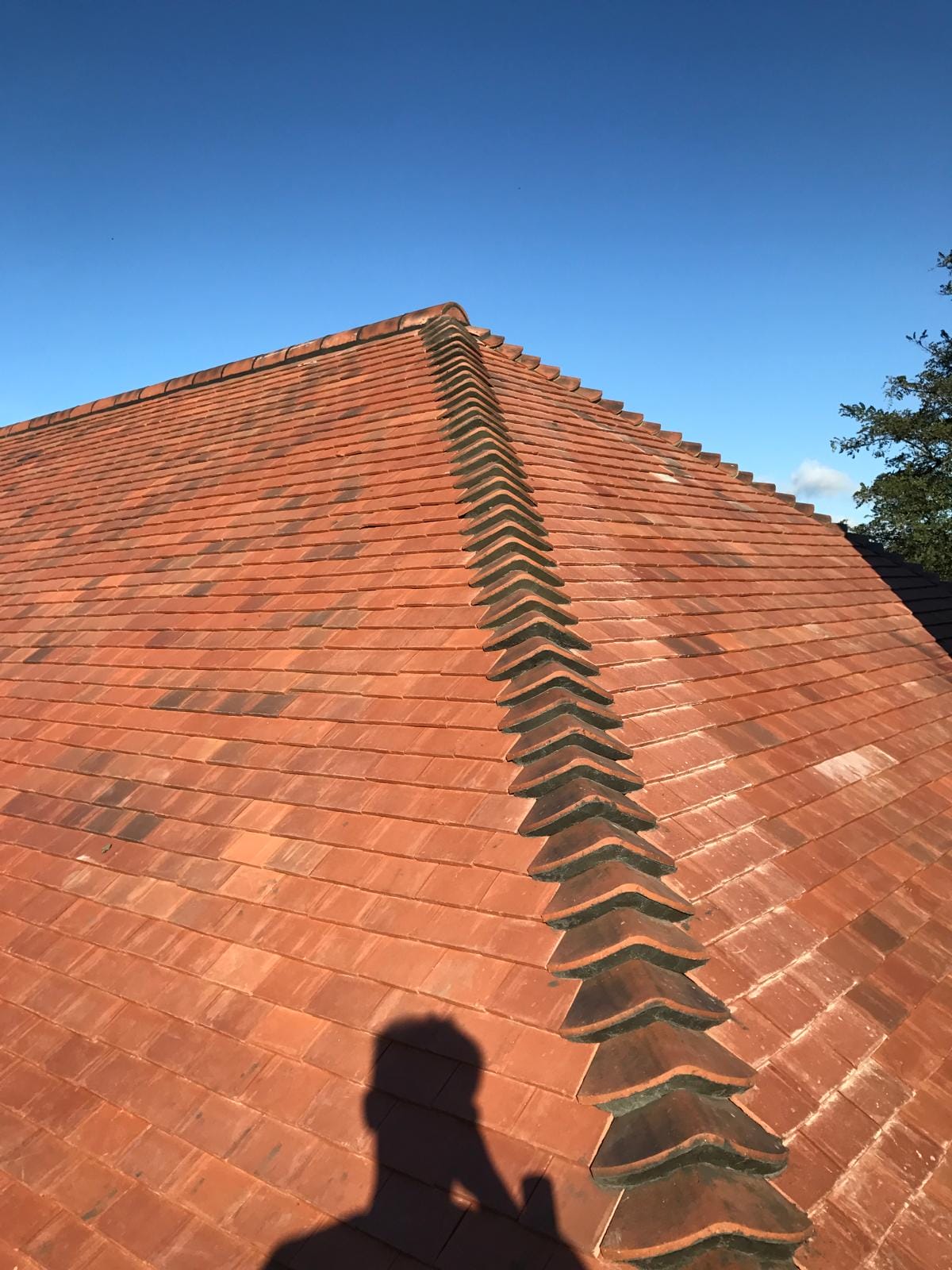 Terracotta clay tile roof with a central ridge line under a bright blue sky.