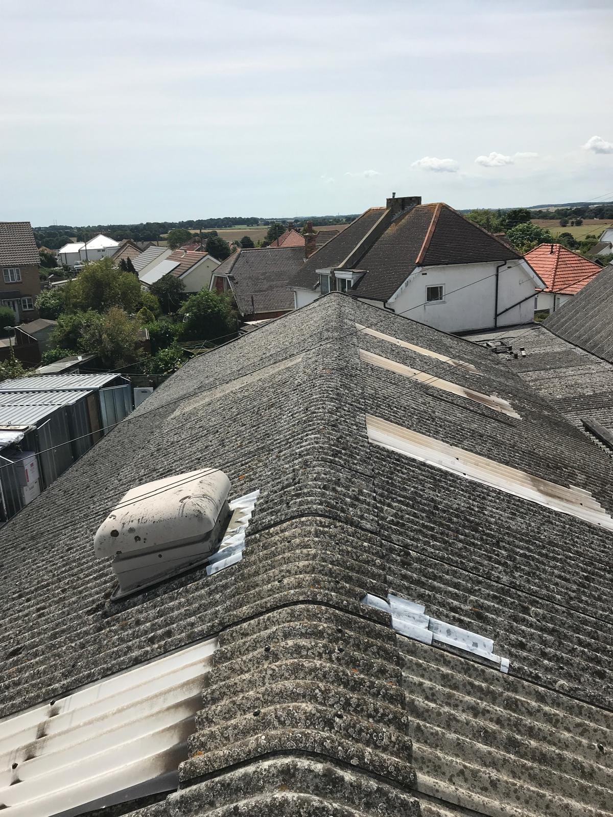 Rooftop view of a suburban neighborhood with grey pitched roofs and a skylight, under a clear sky